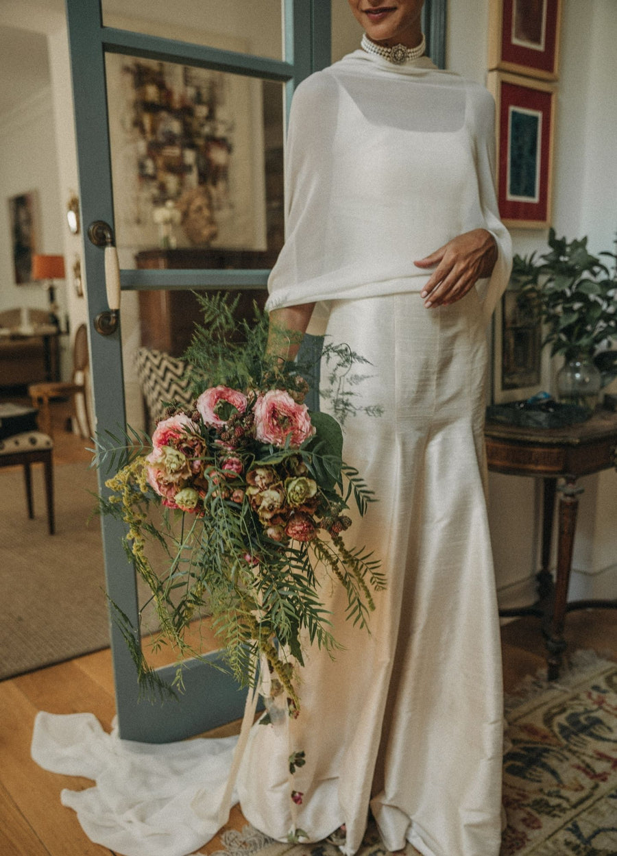 Vestido de novia con capa de gasa y ramo de flores